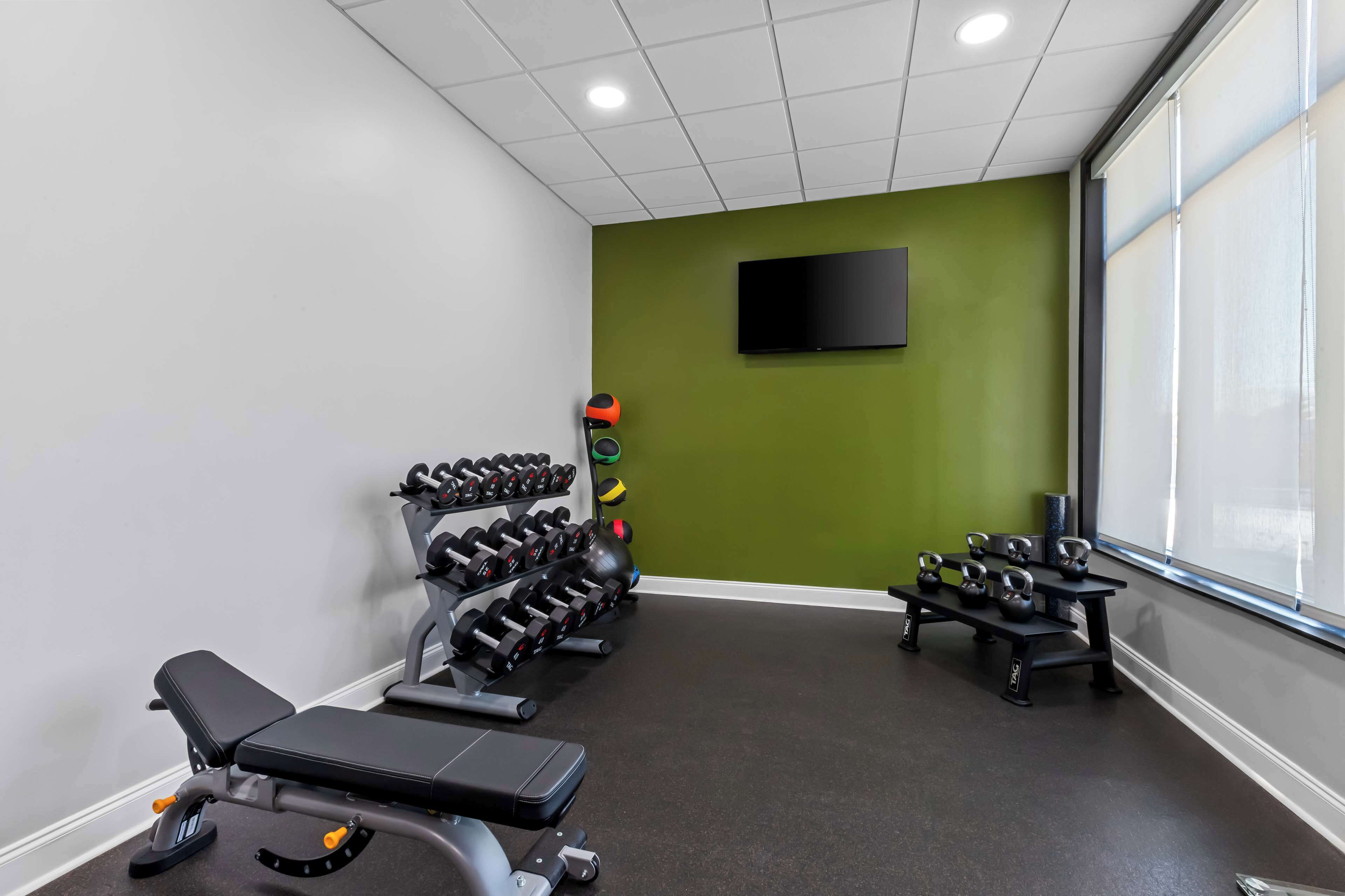 Un gimnasio con equipo de levantamiento de pesas, una banca y un televisor en la pared.