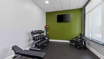 Un gimnasio con equipo de levantamiento de pesas, una banca y un televisor en la pared.