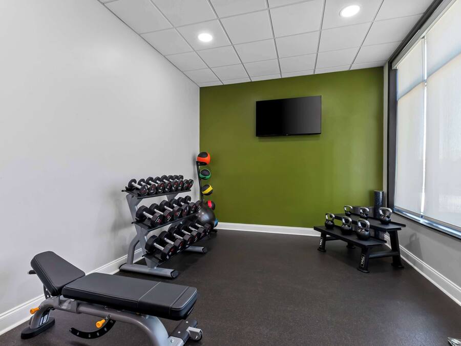 Un gimnasio con equipo de levantamiento de pesas, una banca y un televisor en la pared.