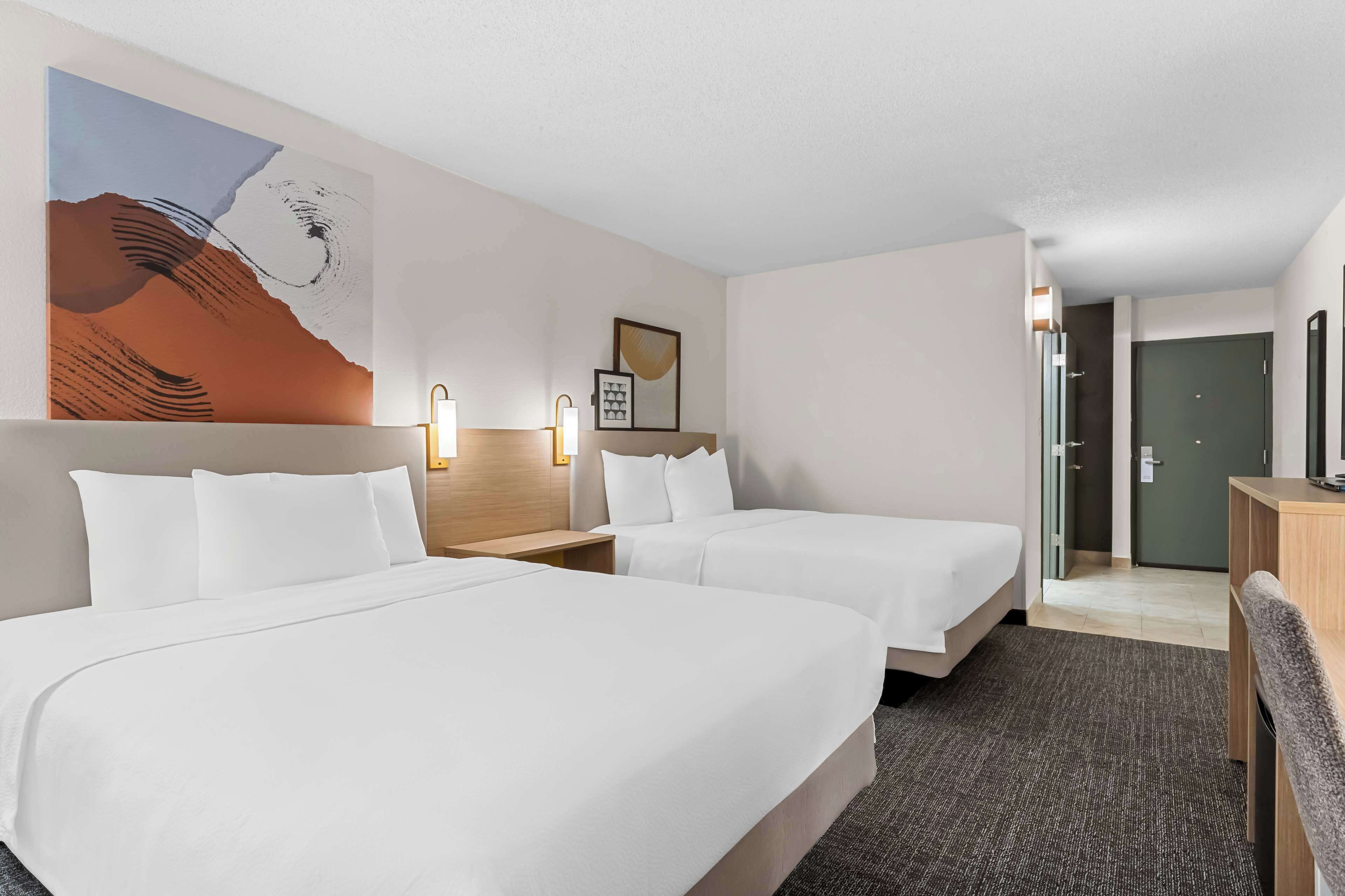 A hotel room with two beds, a large abstract painting on the wall, and a desk with a chair.