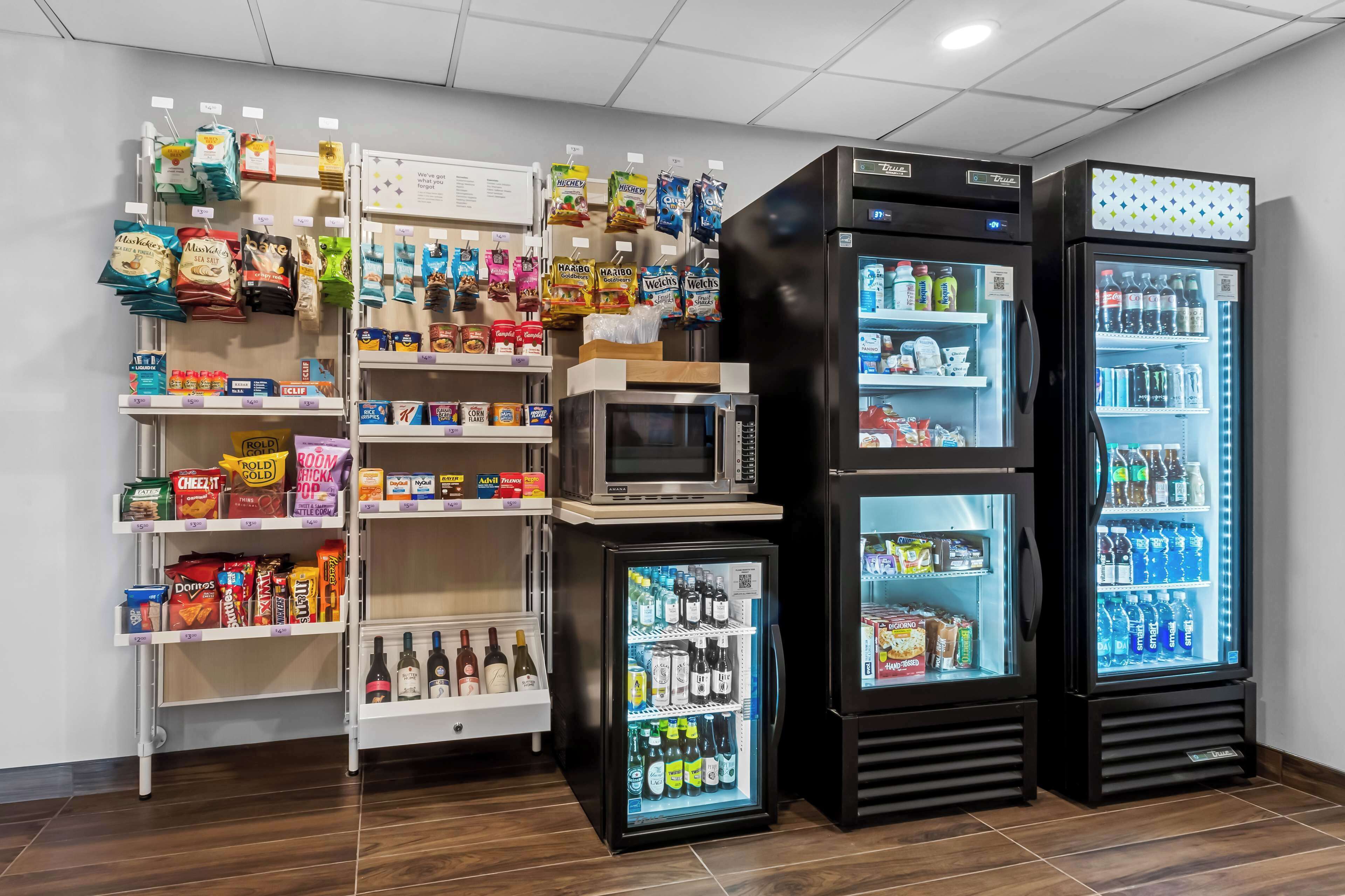A store with shelves stocked with snacks, a microwave, and refrigerated display cases containing beverages and snacks.