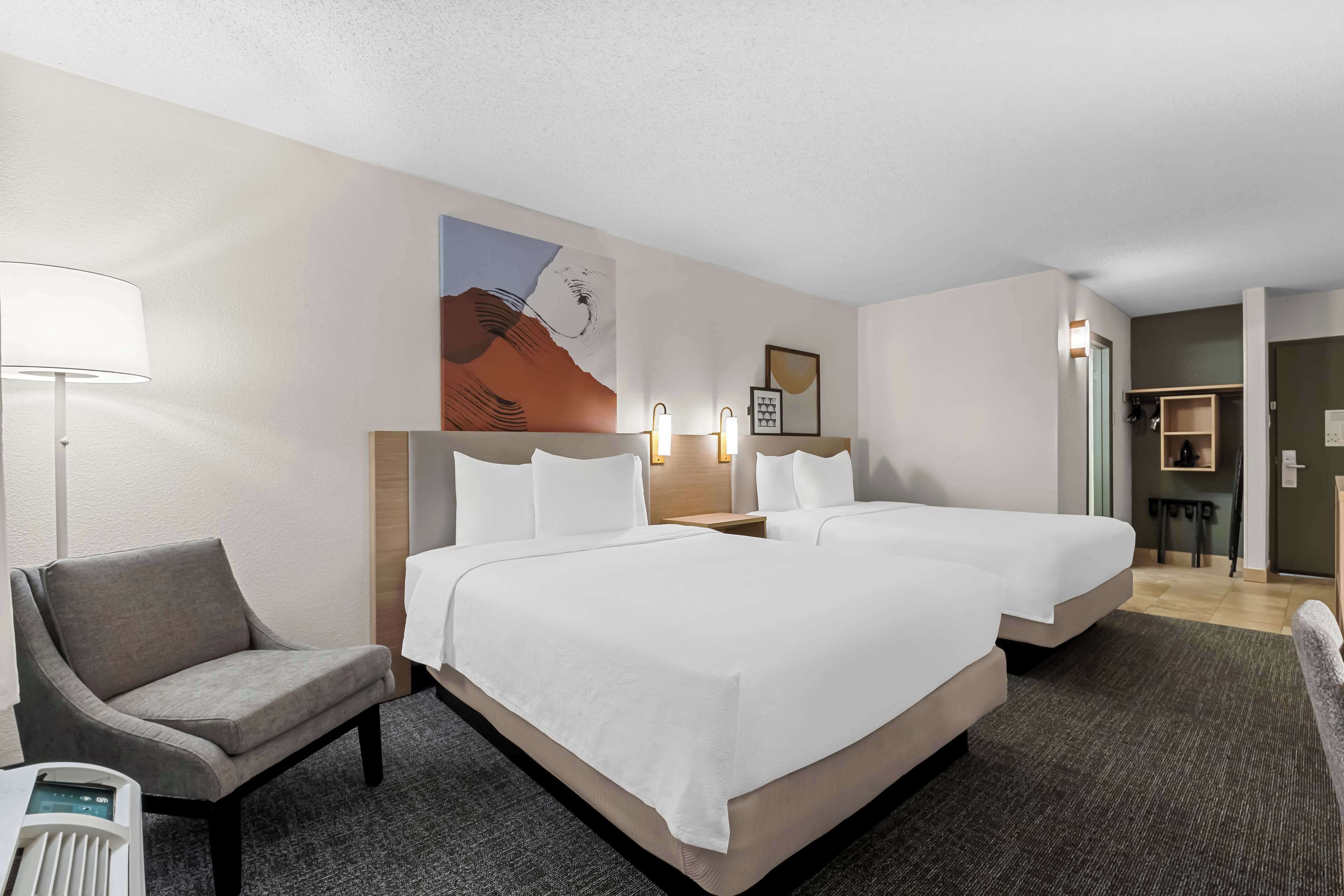 A hotel room with two beds, a chair, a desk, and a painting on the wall.