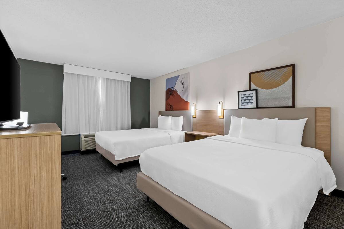 A hotel room with two beds, a desk, a TV, and artwork on the walls.