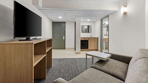 Uma sala de estar moderna com televisão de tela plana, estantes de madeira, um sofá cinza e uma pequena mesa.