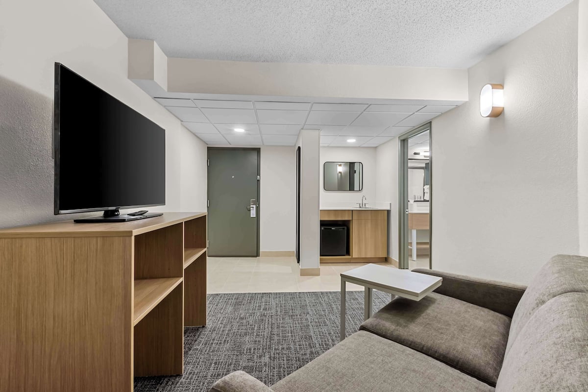 A modern living room with a flat-screen TV, wooden shelving, a gray sofa, and a small table.