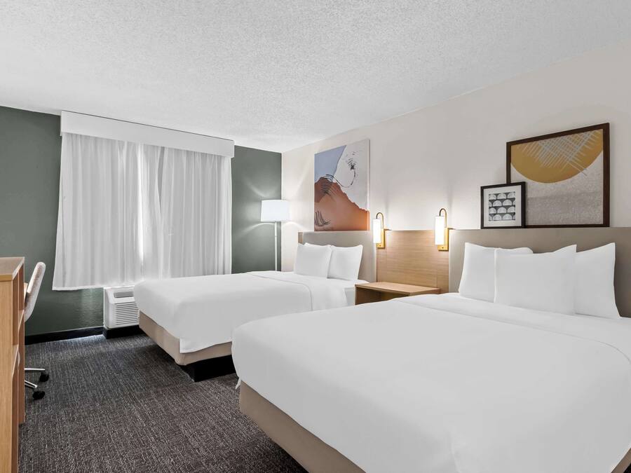 Une chambre d’hôtel avec deux lits, un bureau, une chaise, une lampe et des œuvres d’art accrochées aux murs.