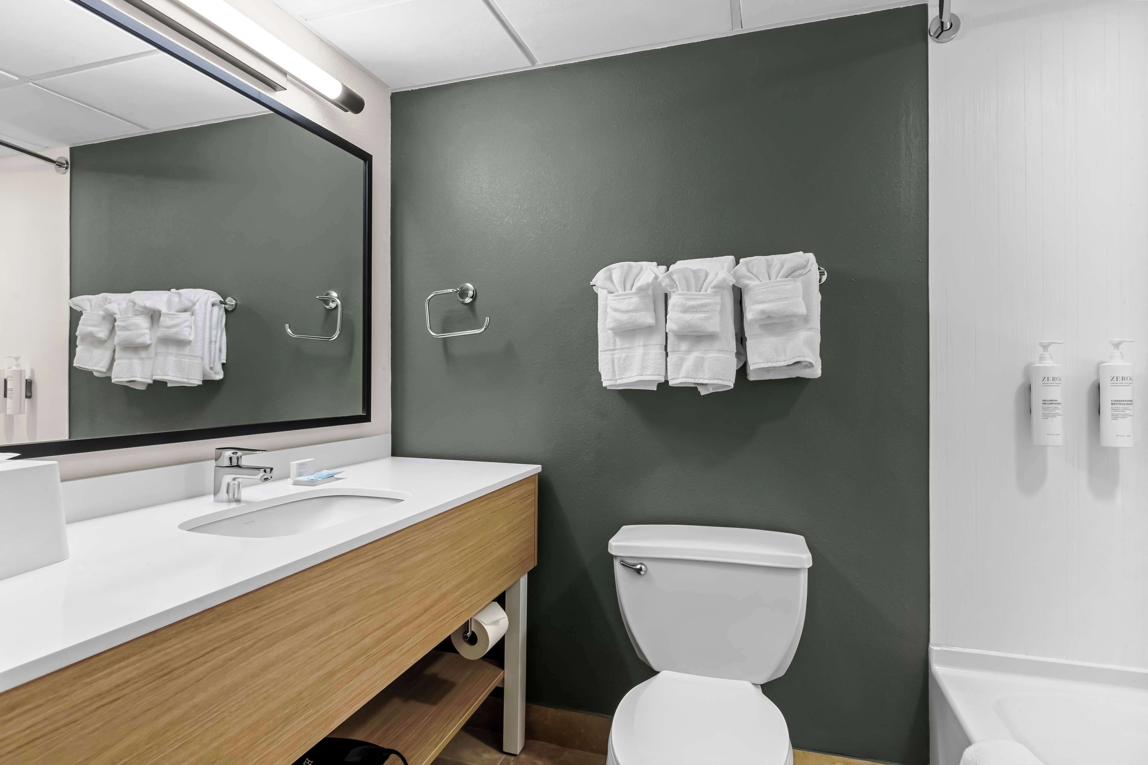 A modern bathroom with a white sink, mirror, and toilet. There are two towel racks with white towels hanging.
