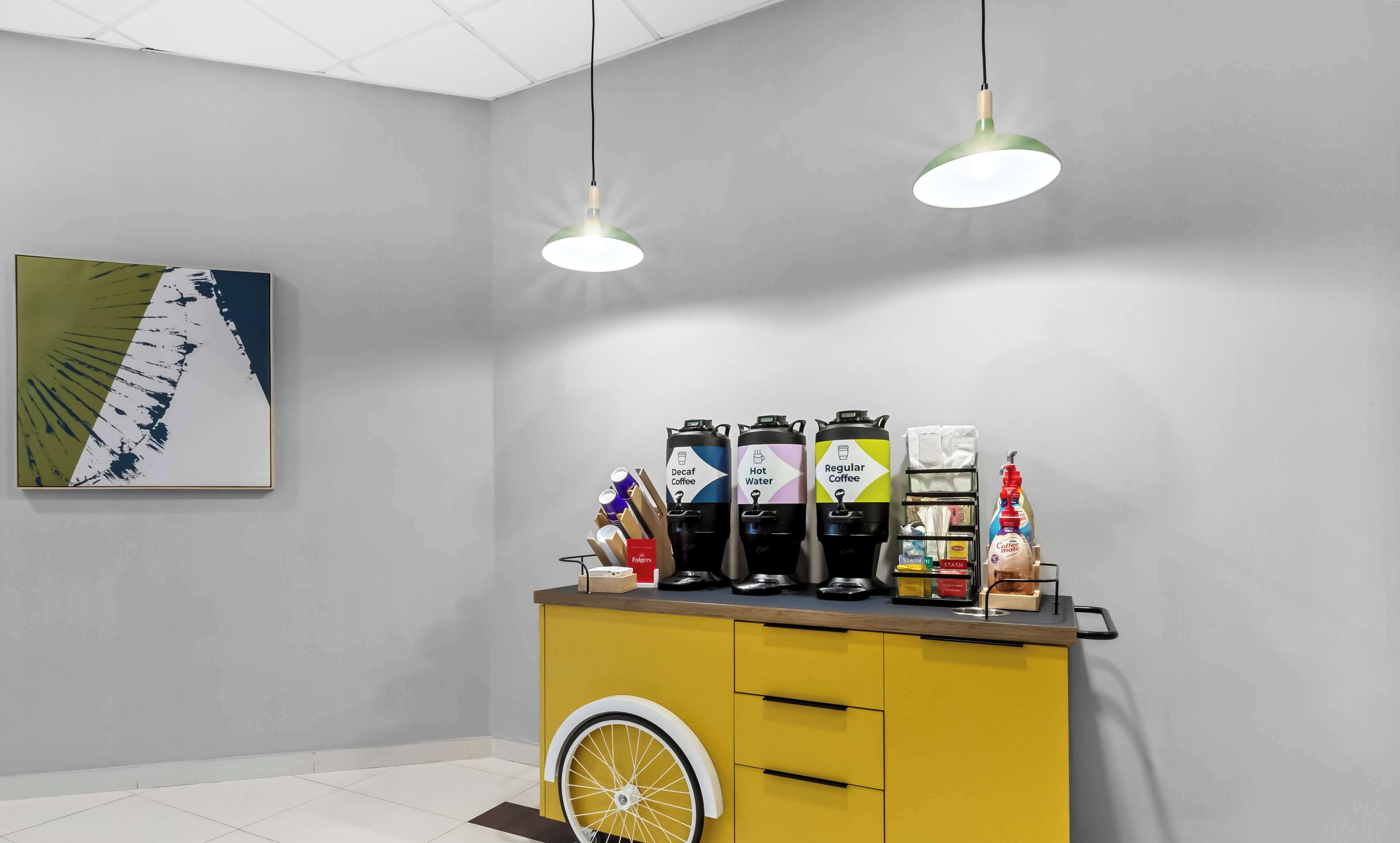 A modern bar area with a yellow counter, three coffee dispensers, and a wheelchair-accessible design.