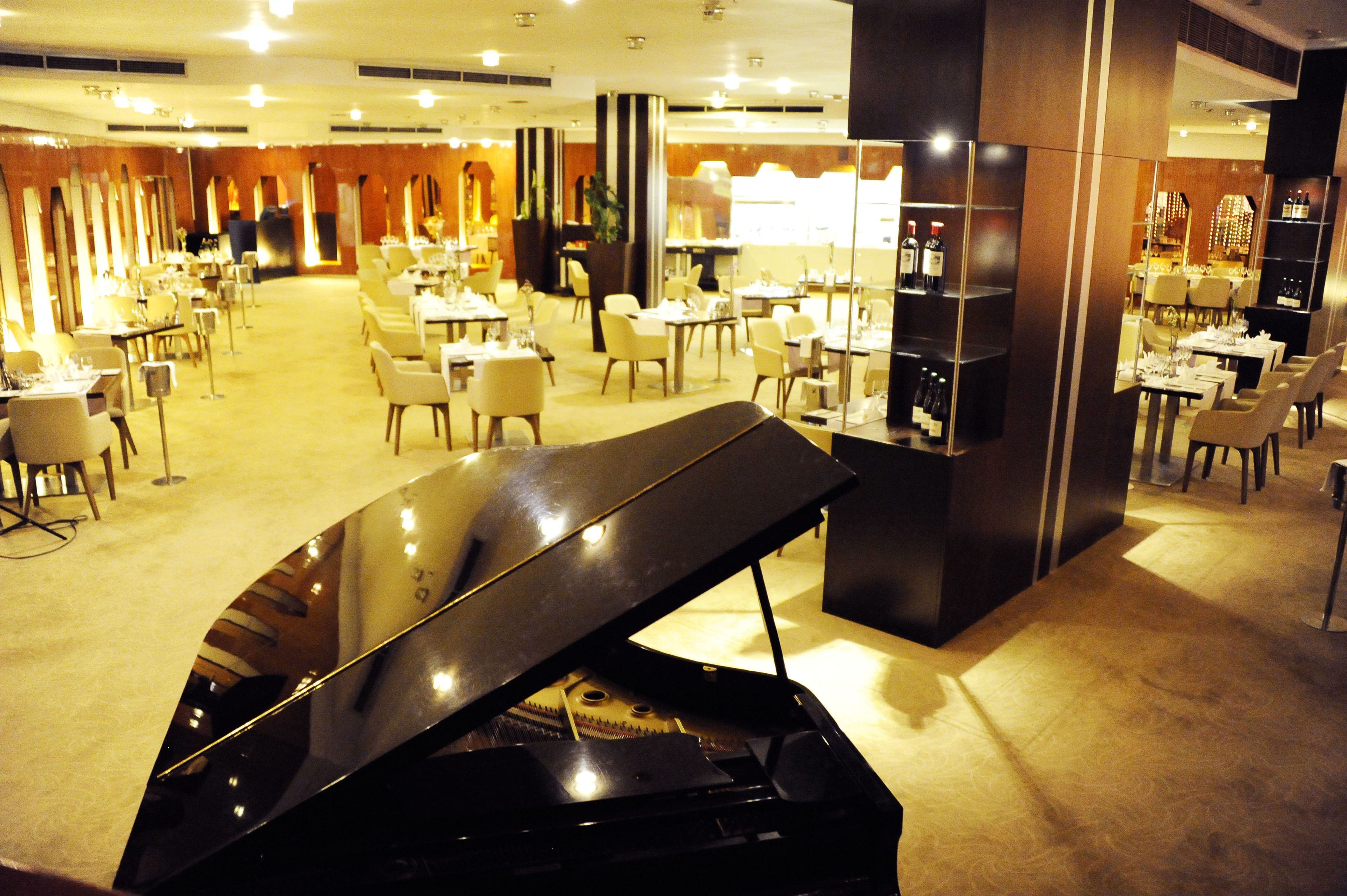 A spacious hotel lobby with a grand piano, multiple dining areas, and a wine bar.