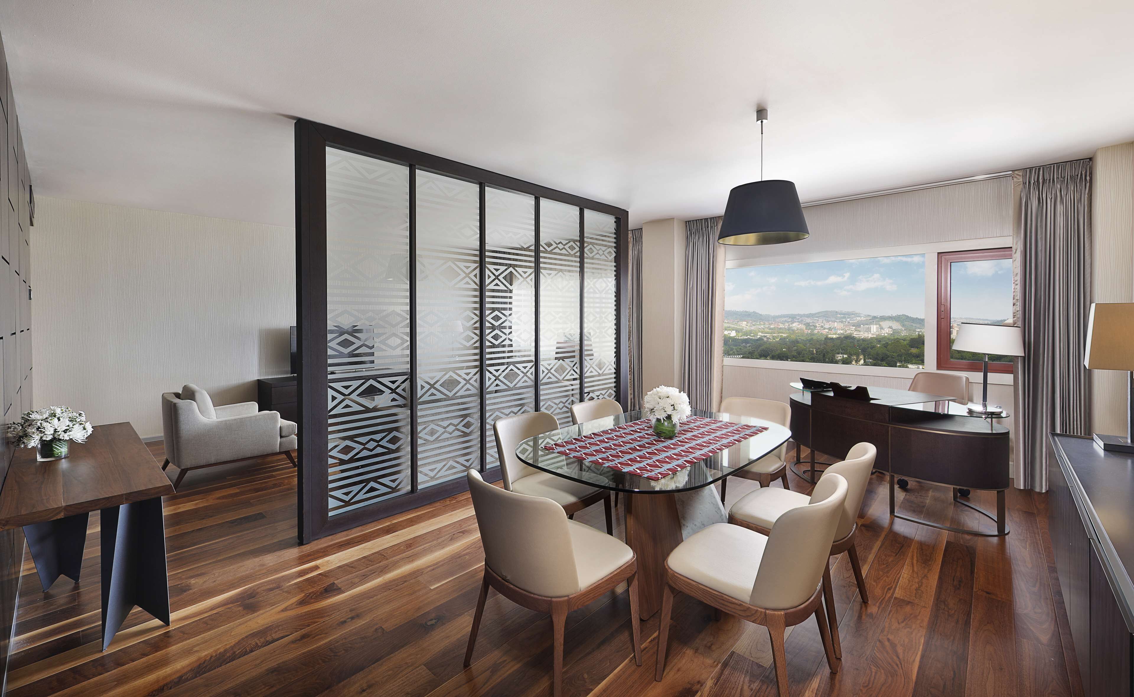 Ett modernt hotellrum med en matplats, en soffa, ett skrivbord och ett stort fönster med utsikt över staden.