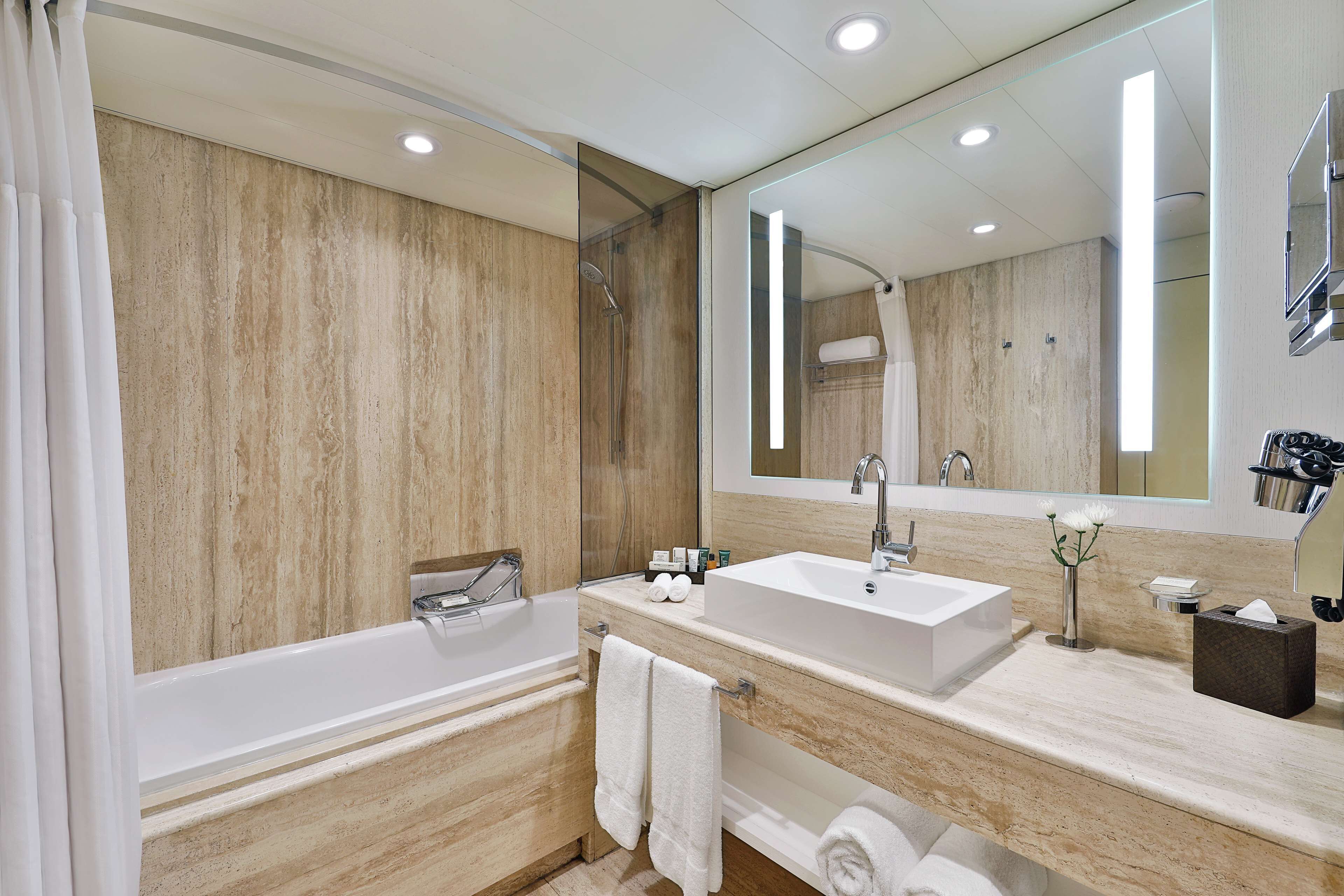 A modern bathroom with a bathtub, two sinks, a large mirror, and a shower.