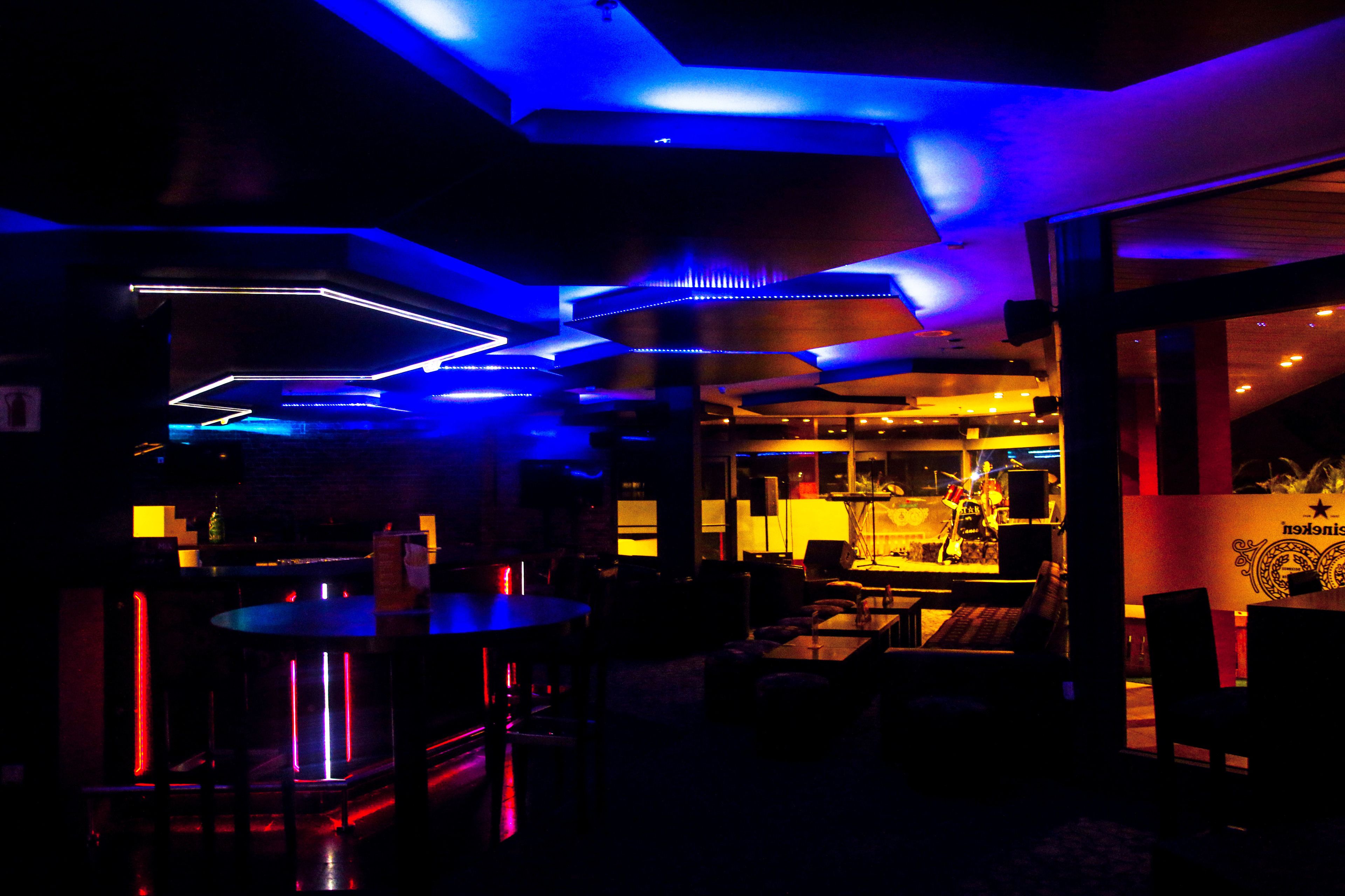 A dimly lit bar area with neon lights, tables, and chairs.