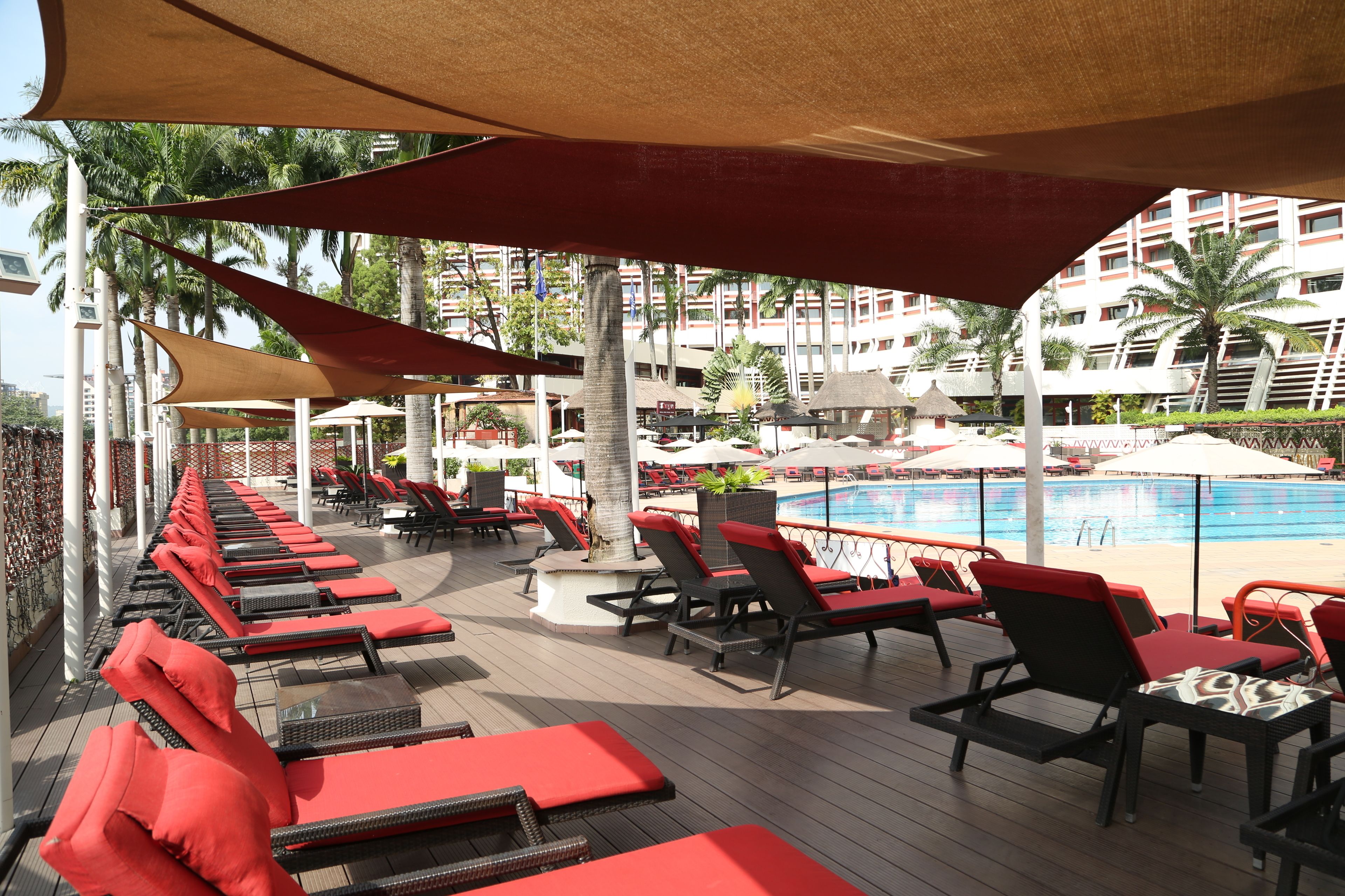 A poolside area with sun loungers and umbrellas, a pool, and a view of a building in the background.