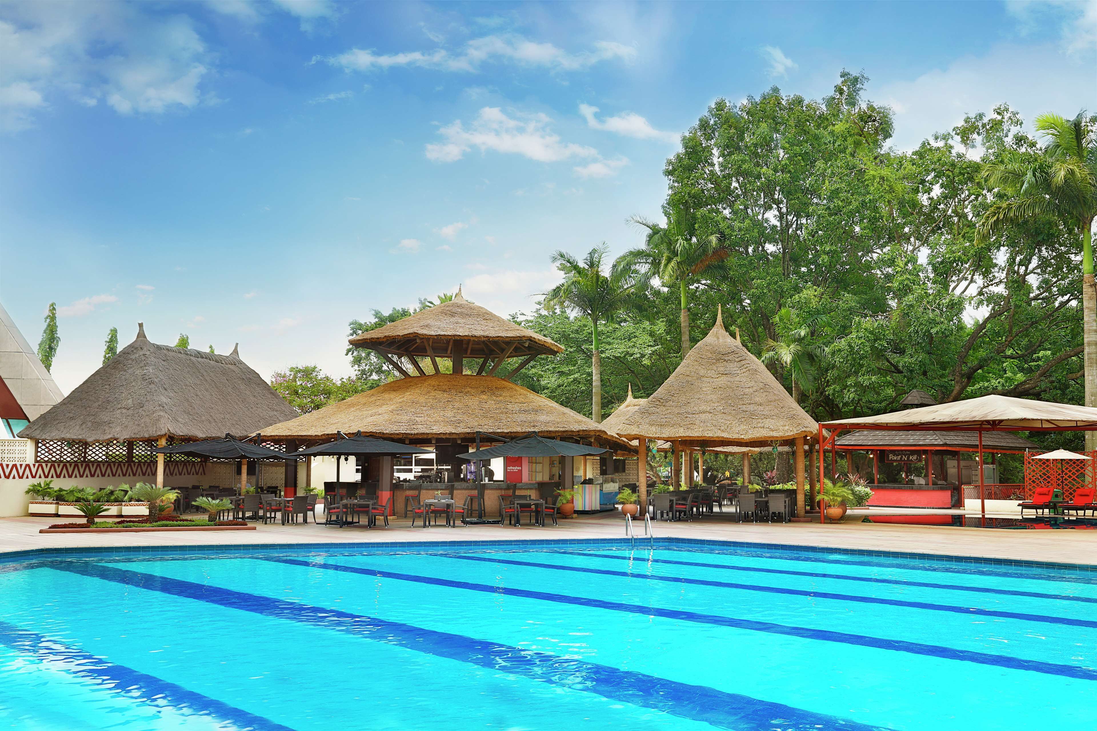 A swimming pool with thatched-roof structures and seating areas.