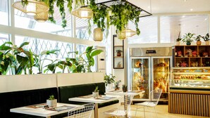 A modern cafe with green cushioned seating, metal chairs, hanging plants, and a bakery display. - Transcorp Hilton Abuja (Abuja)