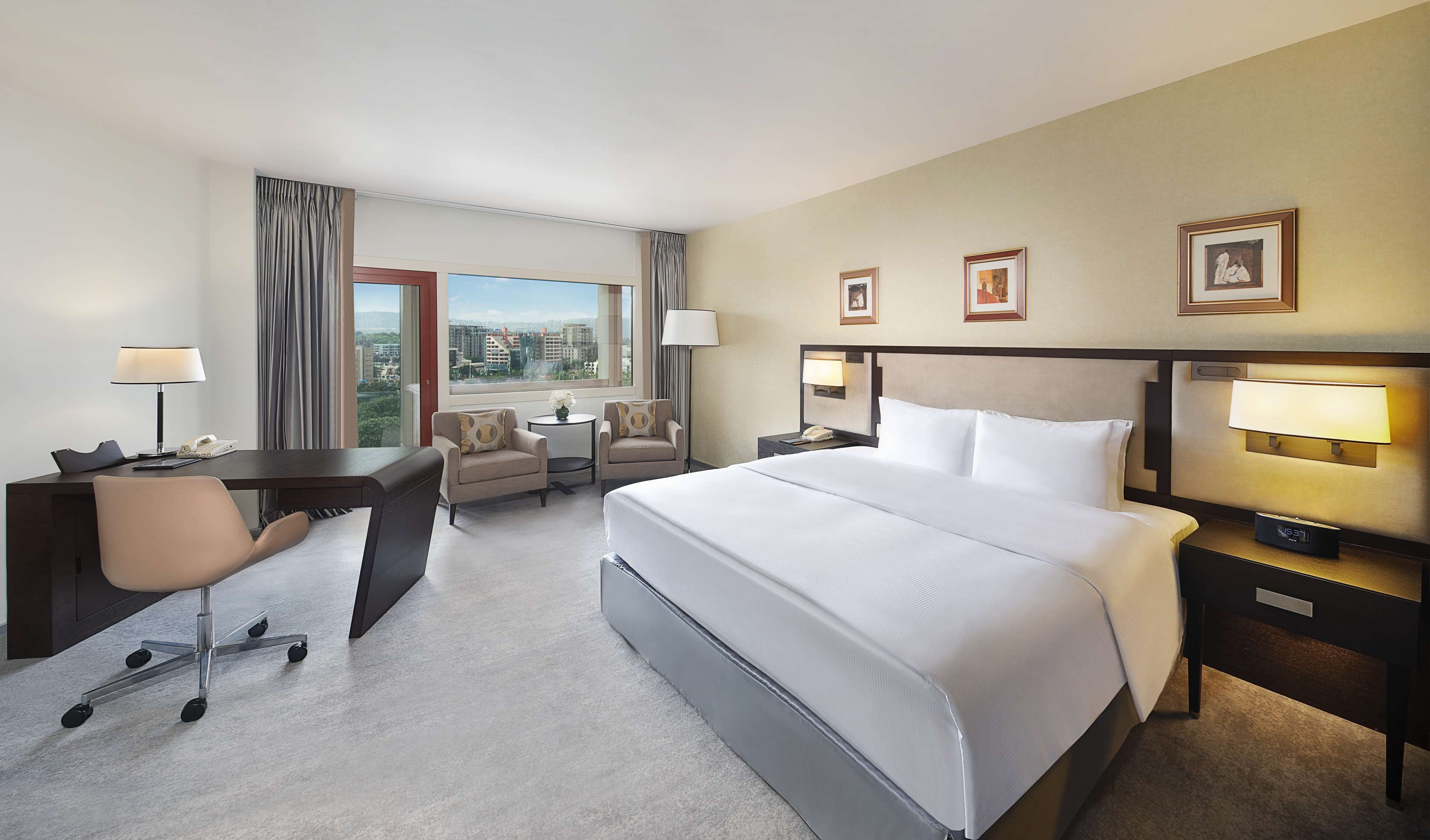 A hotel room with a large bed, a desk, a chair, and a view of the city.