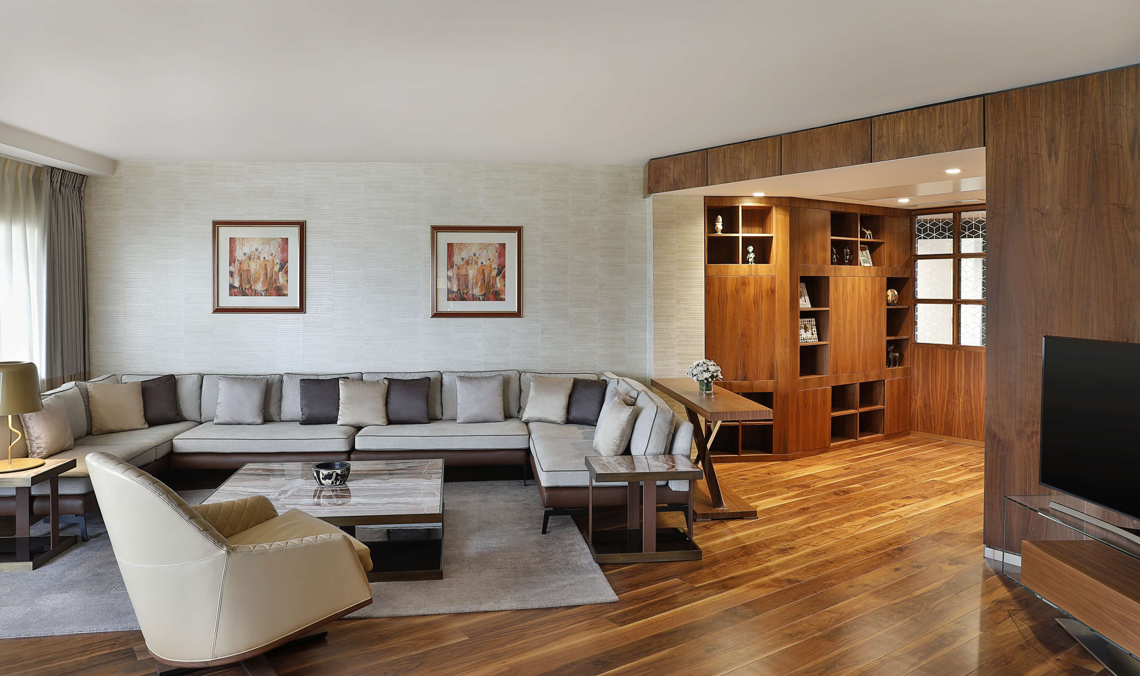 A modern living room with a sectional sofa, a glass coffee table, a leather armchair, a wooden entertainment unit, and a flat-screen TV.