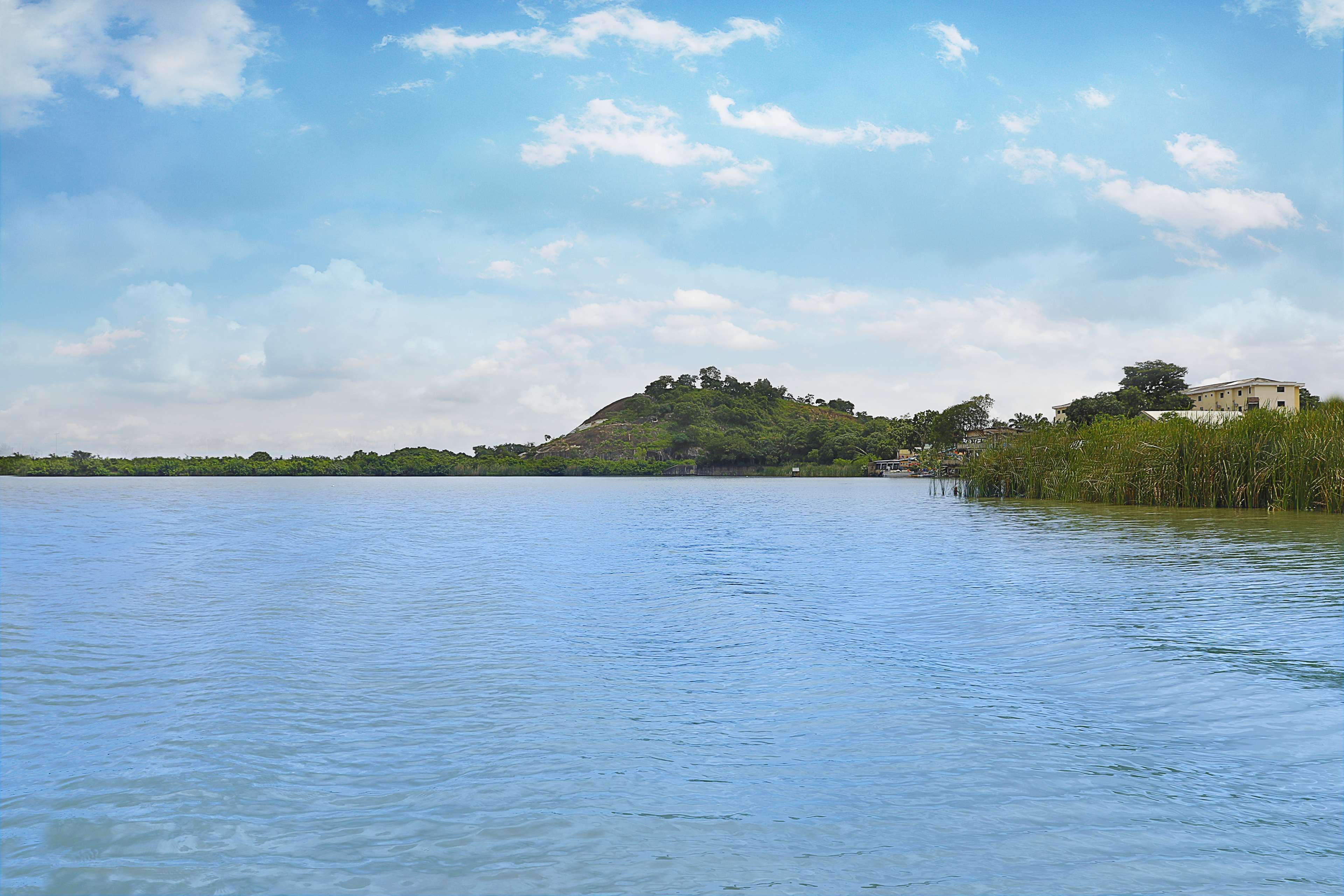 A calm lake with a small hill and a building on the right.
