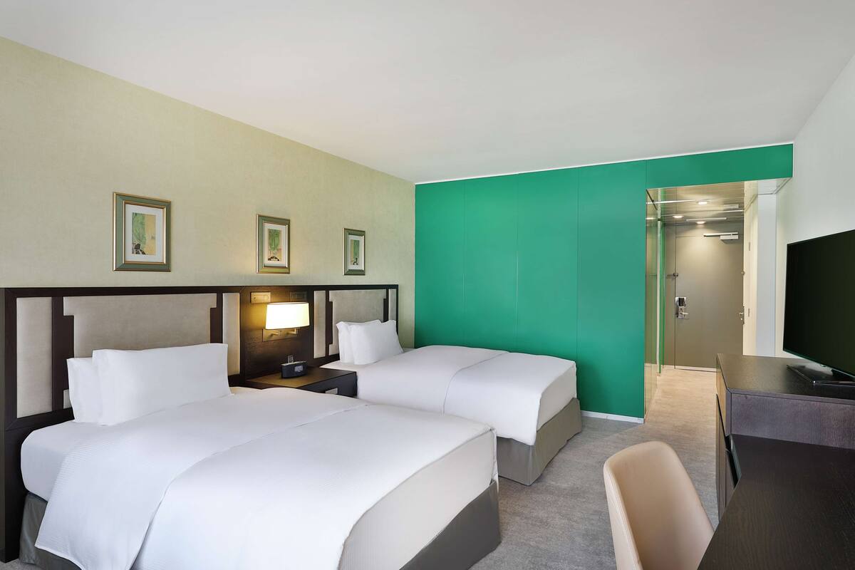 A hotel room with two beds, a desk, a chair, and a television.