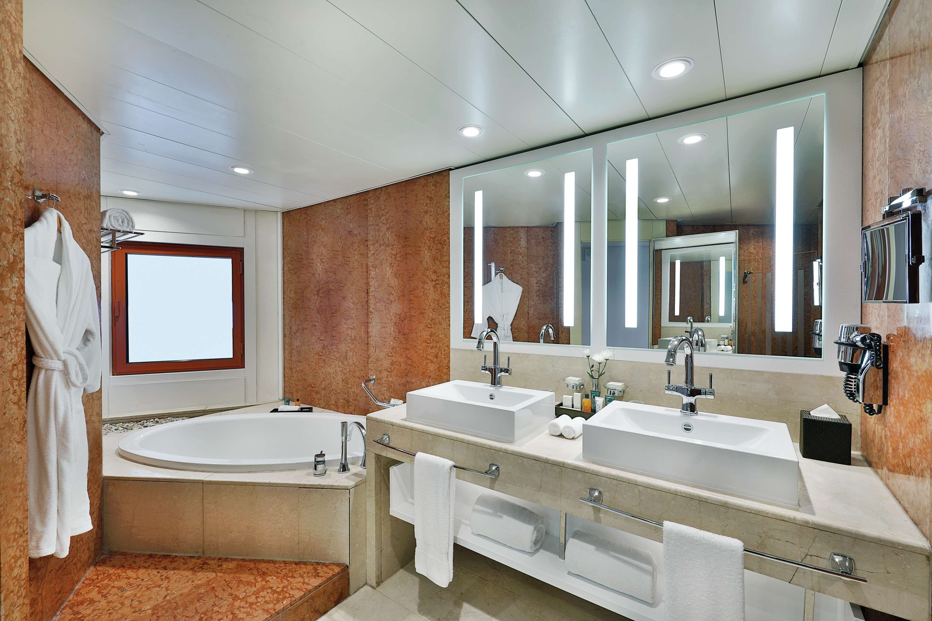 A modern bathroom with a large bathtub, two sinks, and a large mirror.