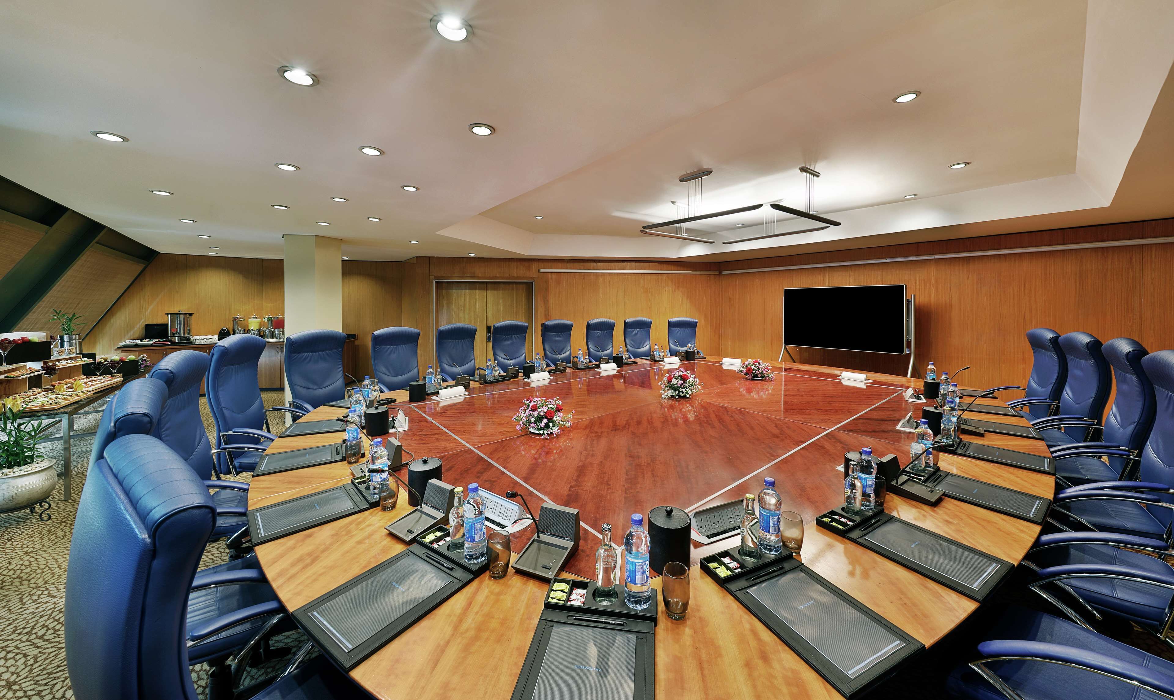 Una sala de conferencias con una gran mesa ovalada, sillas azules y un televisor de pantalla plana.