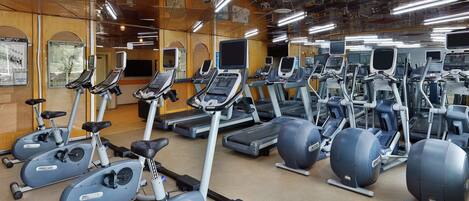 A gym with multiple exercise machines, including treadmills and stationary bikes, arranged in rows.