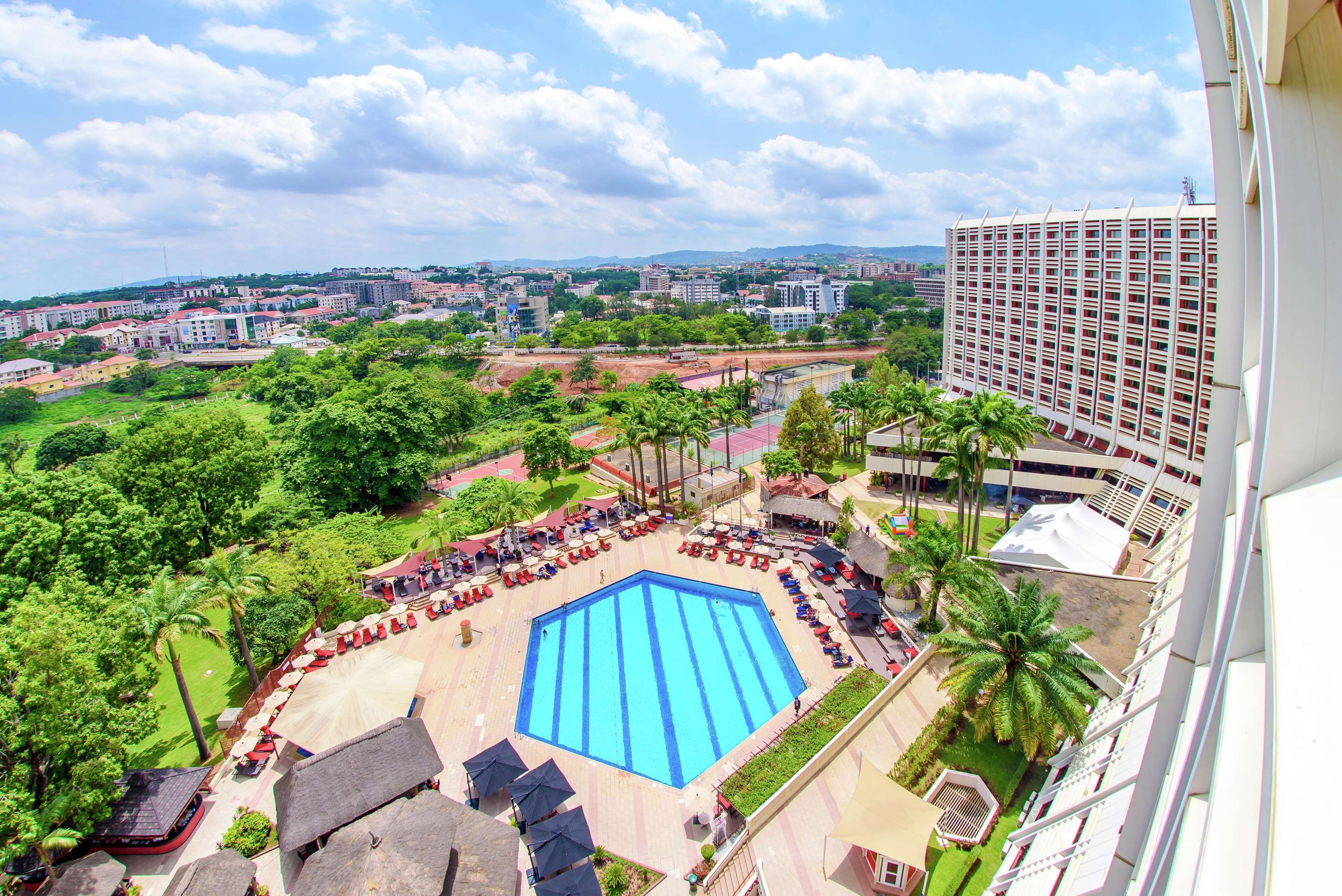 Ein Swimmingpool, umgeben von Liegestühlen und Sonnenschirmen, mit Blick auf eine Stadtlandschaft im Hintergrund.