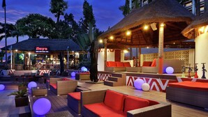 An outdoor lounge area with wicker furniture, red cushions, and thatched umbrellas. - Transcorp Hilton Abuja (Abuja)