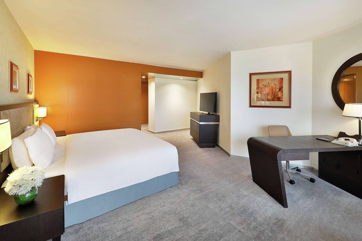 A hotel room with a bed, desk, chair, TV, and a desk lamp.