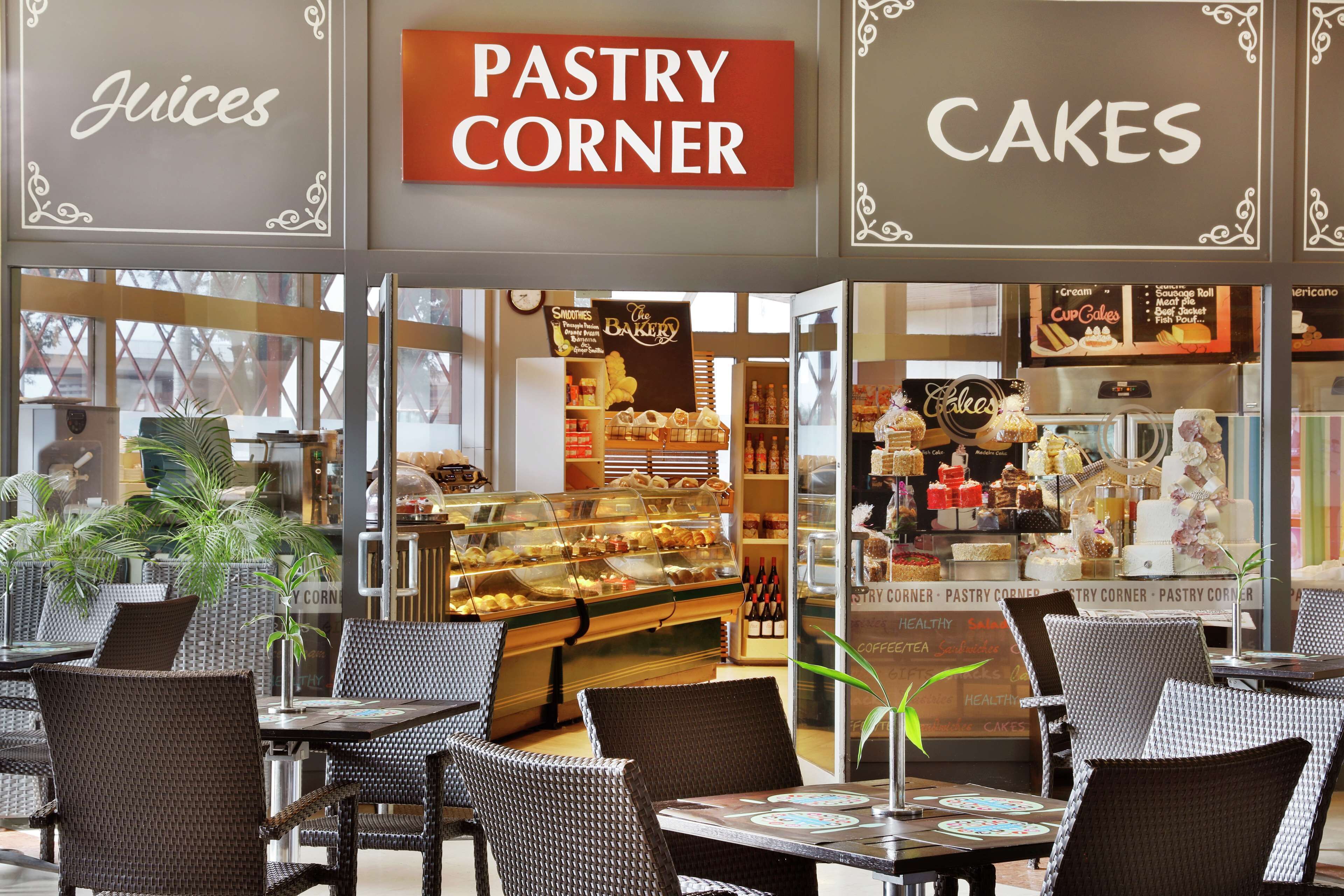 A cafe with wicker chairs, a pastry corner, and a display of cakes and pastries.