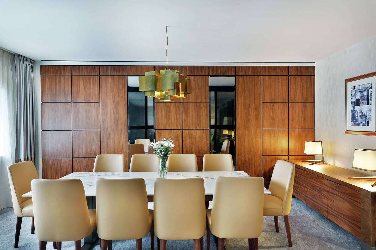 A modern dining area with a rectangular table, six chairs, a vase of flowers, and a wooden partition wall.