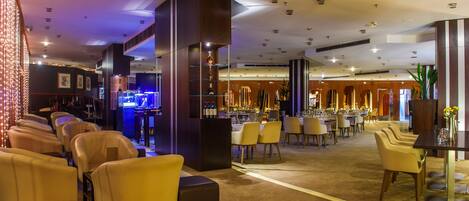 A hotel lobby with a bar area, seating arrangements, and a reception desk.