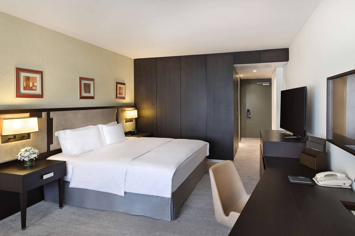 A hotel room with a large bed, bedside tables with lamps, a desk with a TV, and a mirror.