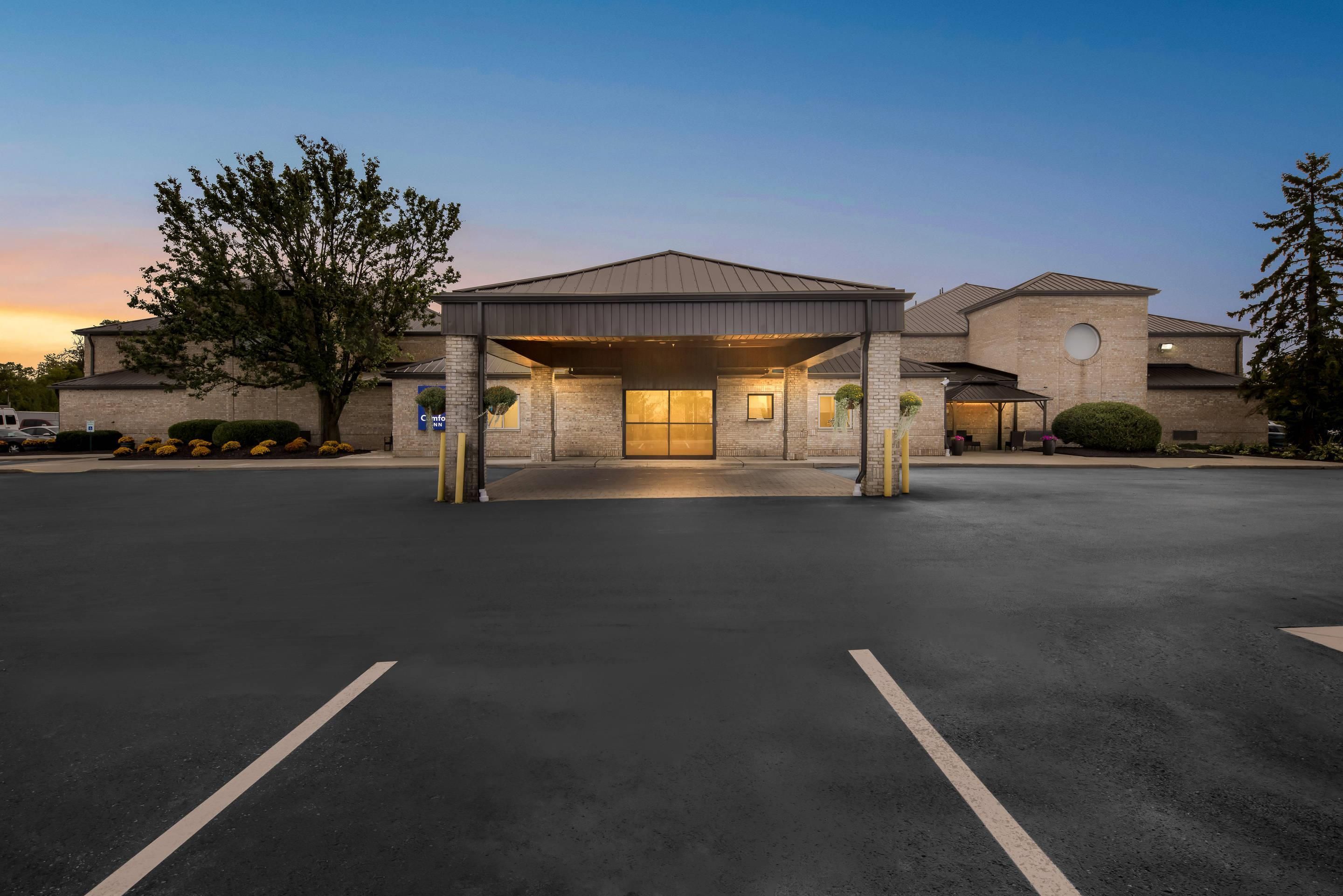 A hotel entrance with a covered waiting area, a brick facade, and a parking lot.