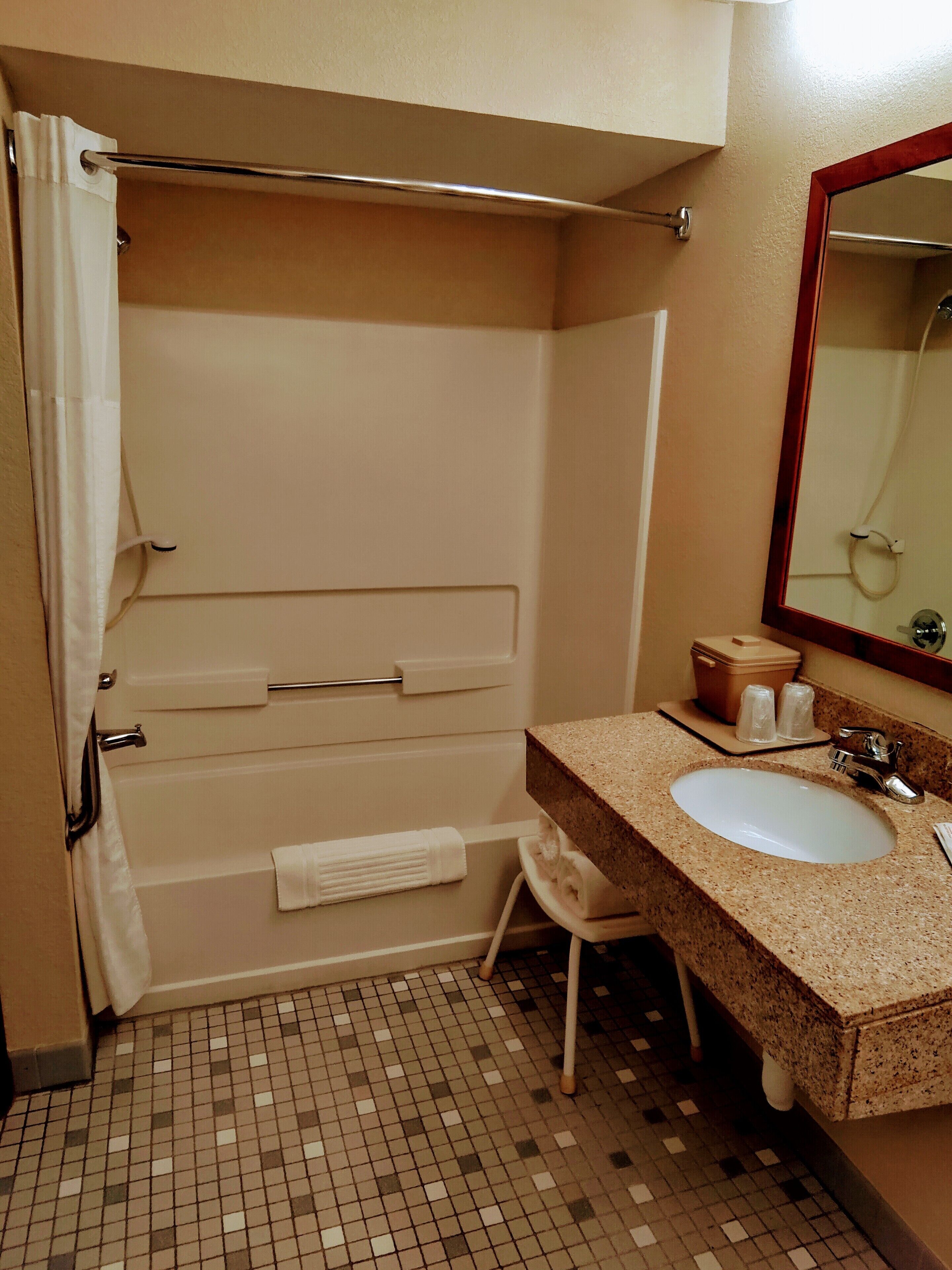 A bathroom with a shower, a sink, a mirror, and a towel rack.
