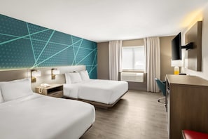 A hotel room with two beds, a desk, a TV, and a window with curtains.