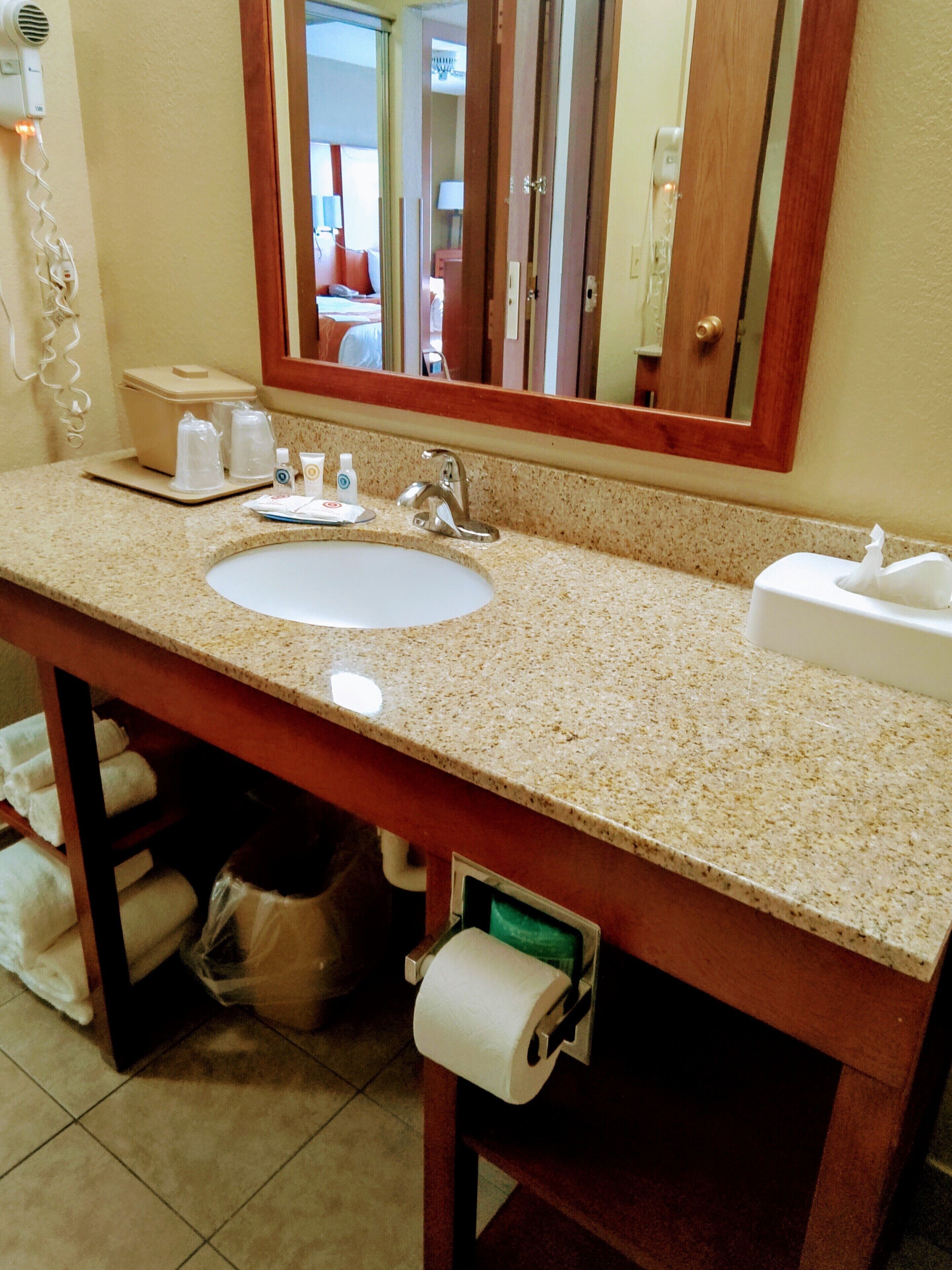 A bathroom with a granite countertop sink, a mirror, a towel rack, and a trash can.