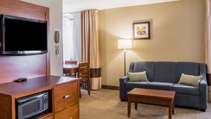 A hotel room with a flat-screen TV, a microwave, a sofa, a coffee table, a desk with a chair, and a lamp. - Comfort Inn Bellefontaine (Bellefontaine)