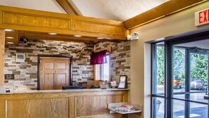 A reception area with a stone wall, wooden paneling, a reception desk, and an exit sign. - Comfort Inn Bellefontaine (Bellefontaine)