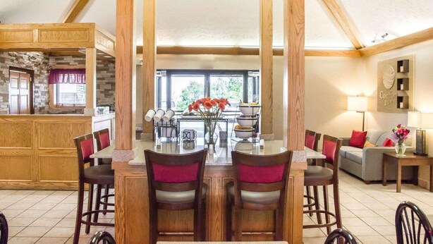 A spacious dining area with a high ceiling and exposed wooden beams, a central island with a vase of flowers, and a view of the outdoors through large windows. - Comfort Inn Bellefontaine (Bellefontaine)