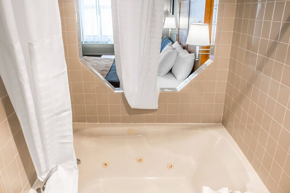 A bathroom with a bathtub, a mirror, and a window.