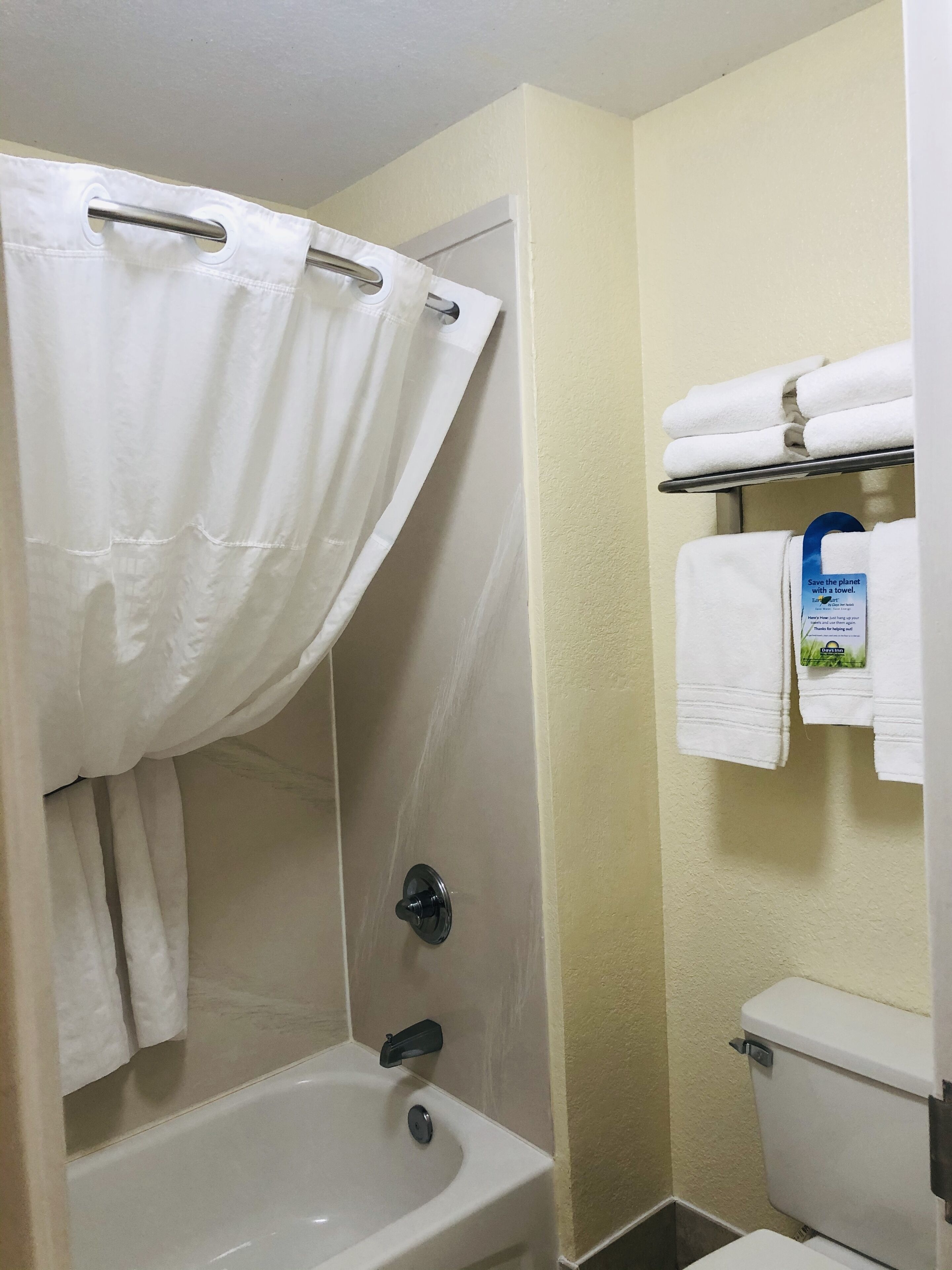 Un baño con cortina de ducha, lavamanos, inodoro y toallero con toallas dobladas.