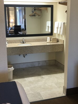 Une salle de bain avec un lavabo doté d’un plan de travail en granit, un miroir, un porte-serviettes et des toilettes.