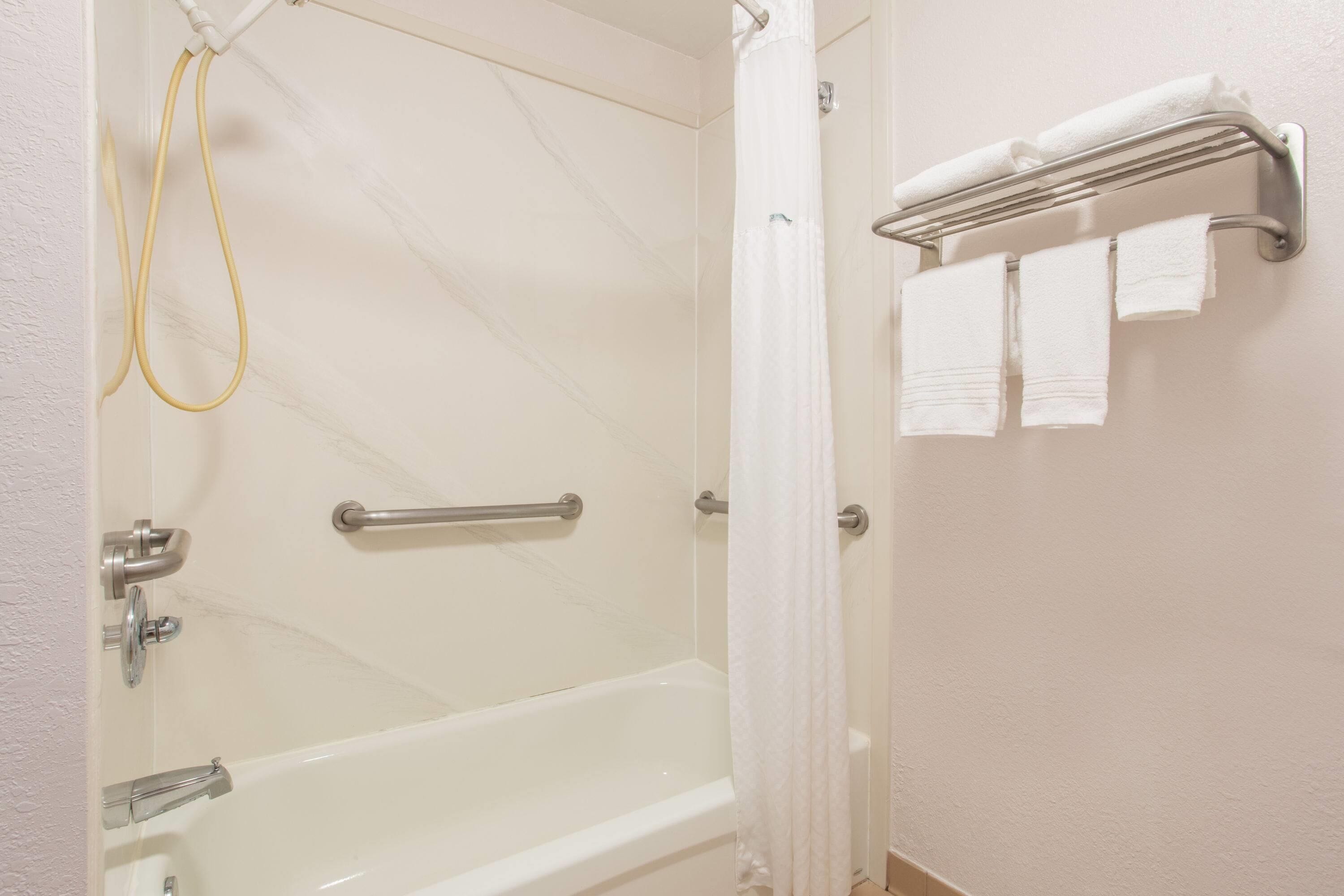 A bathroom with a bathtub, a shower, a towel rack with towels, and a handrail.