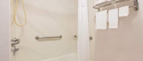 A bathroom with a bathtub, a shower, a towel rack with towels, and a handrail.