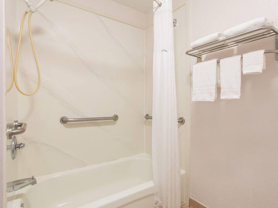 A bathroom with a bathtub, a shower, a towel rack with towels, and a handrail.