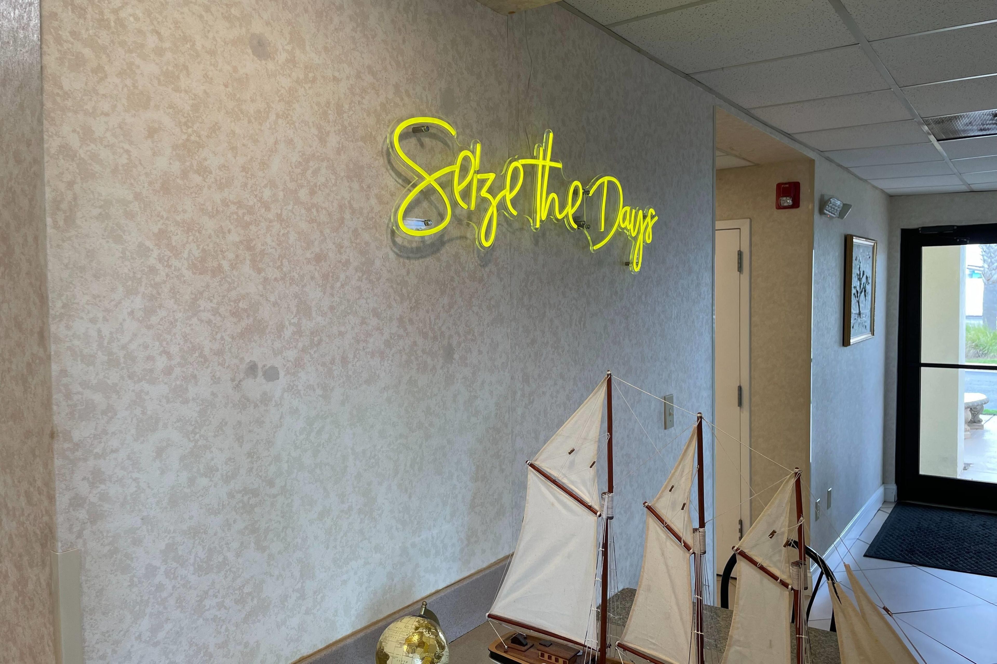 A hallway with a neon sign reading 'Sail the Days' and a model sailboat display.