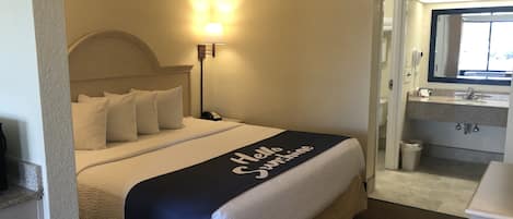 A hotel room with a bed, a nightstand, a lamp, a bathroom with a sink and mirror.