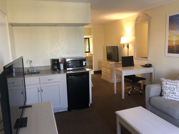 Une chambre d’hôtel compacte comprenant un coin cuisine, un bureau avec une chaise, une télévision et un canapé agrémenté d’un coussin décoratif.
