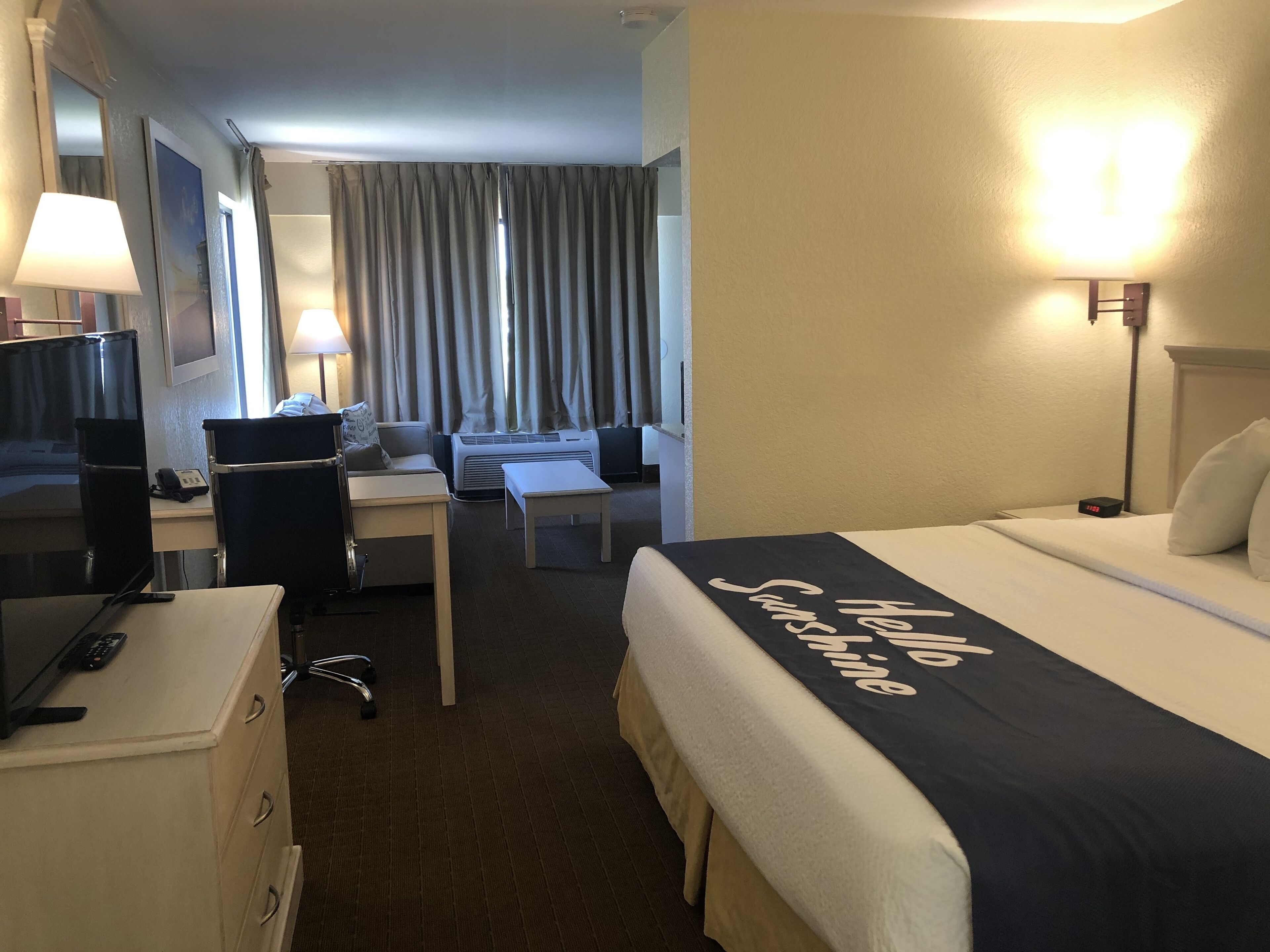 A hotel room with a bed, desk, chair, TV, and lamp.